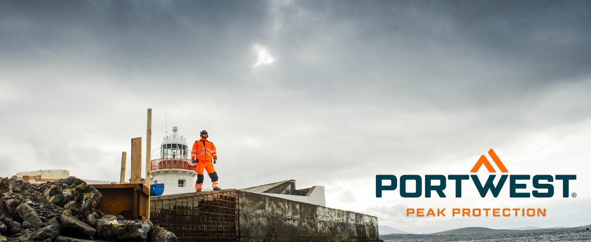 Ein Arbeiter in orangefarbener Warnschutzkleidung steht auf einer felsigen Baustelle neben einem Leuchtturm, mit dem Portwest-Logo und dem Slogan 'Peak Protection' im Bild.