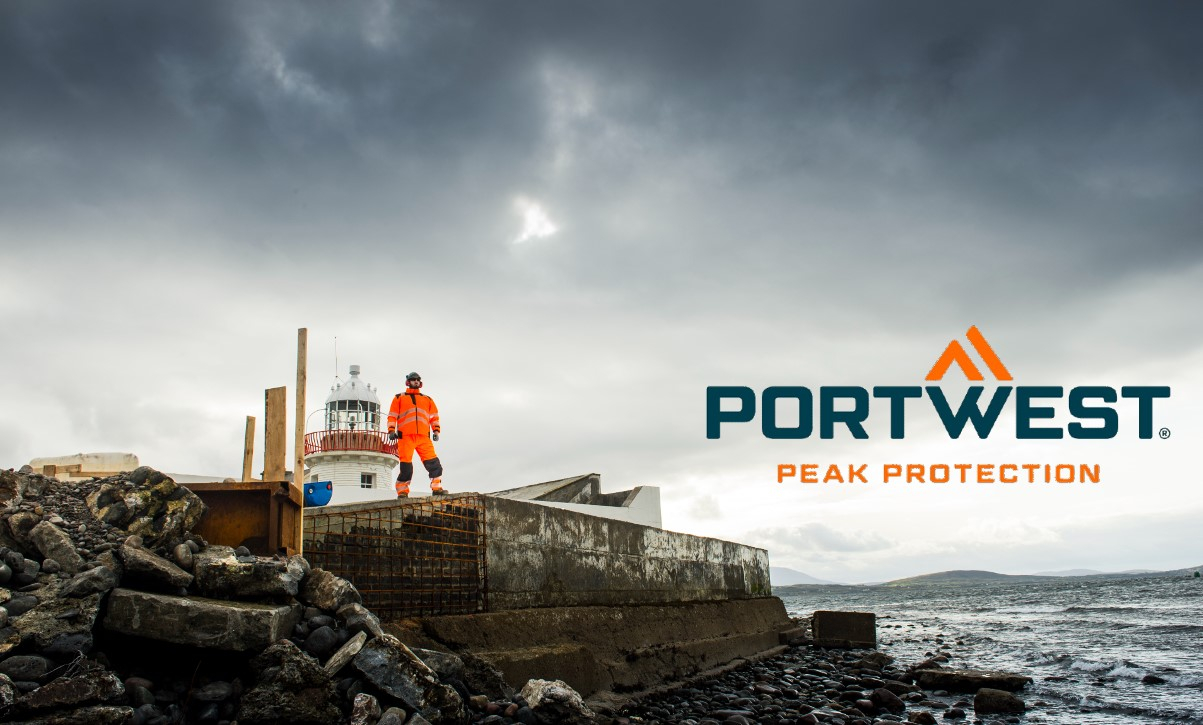 Ein Arbeiter in orangefarbener Warnschutzkleidung steht auf einer felsigen Baustelle neben einem Leuchtturm, mit dem Portwest-Logo und dem Slogan 'Peak Protection' im Bild. Hinterlegt ist ein Link, der zu unserer Multinorm-Arbeitskleidung führt.