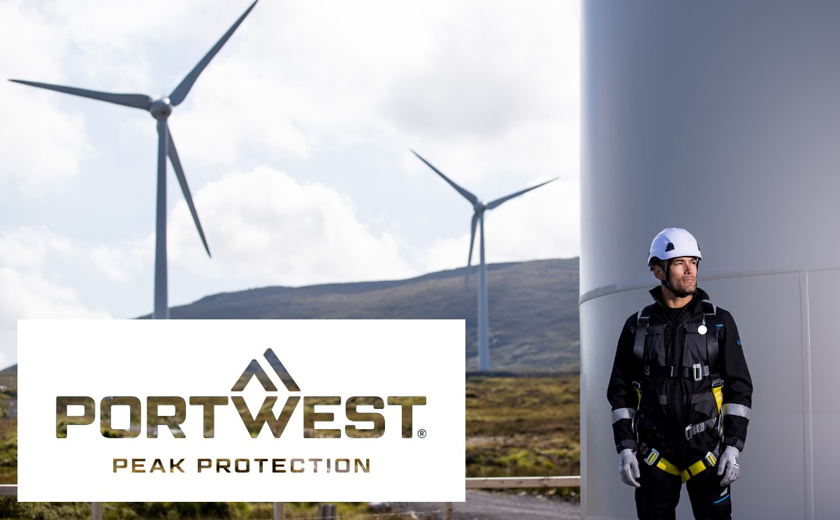 Ein Arbeiter, der eine vollständige Absturzsicherungsausrüstung trägt, steht neben einer Windkraftanlage. Im Hintergrund sind weitere Windturbinen zu sehen. Das Logo der Firma Portwest mit dem Slogan 'Peak Protection' ist im Vordergrund eingeblendet. Ein Link, der zu unserer Absturzsicherung führt, ist hinterlegt.