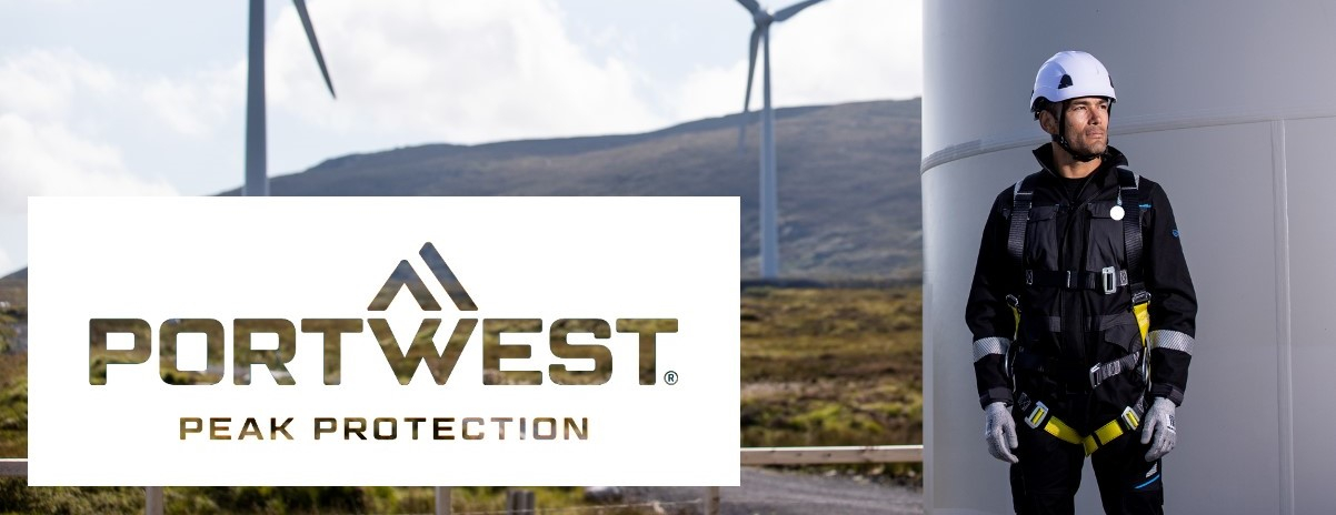 Ein Arbeiter, der eine vollständige Absturzsicherungsausrüstung trägt, steht neben einer Windkraftanlage. Im Hintergrund sind weitere Windturbinen zu sehen. Das Logo der Firma Portwest mit dem Slogan 'Peak Protection' ist im Vordergrund eingeblendet.