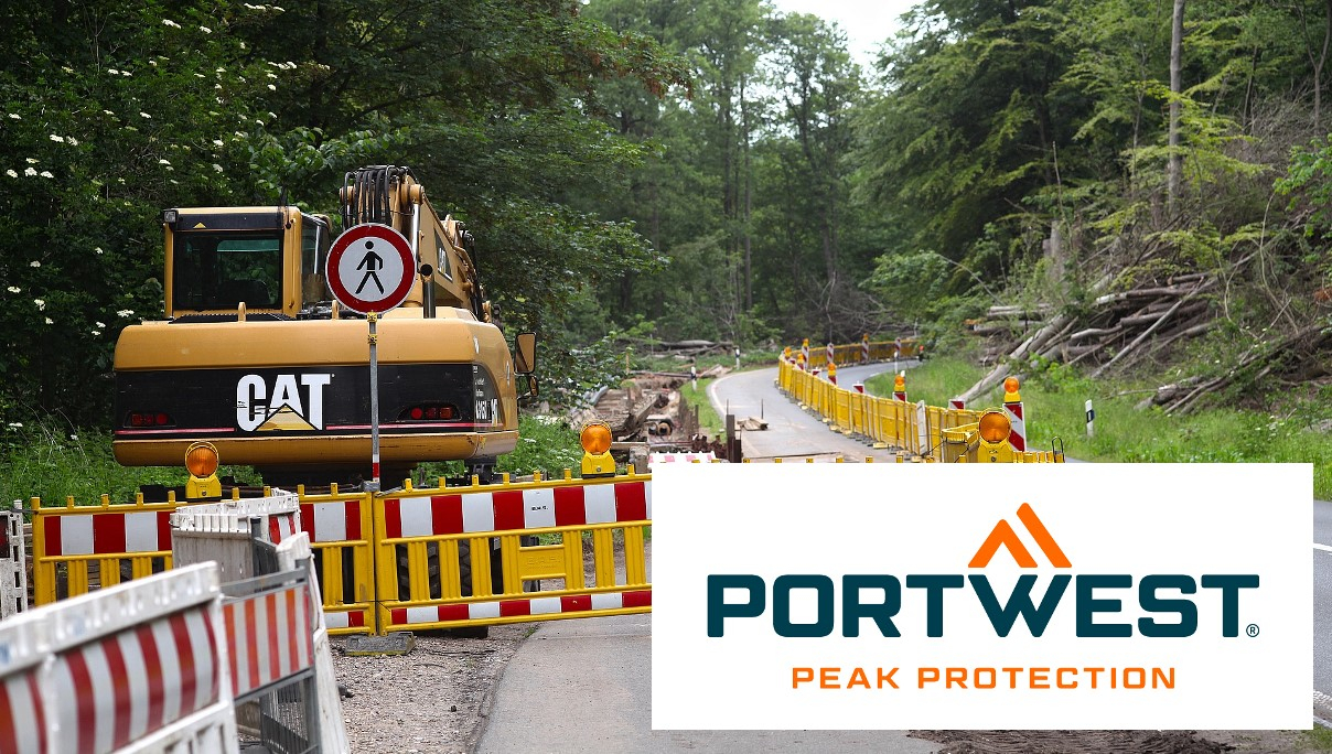 Baustelle an einer Straße im Wald. Eine gelbe Absperrung grenzt die Baustelle ein. Im rechten unteren Bildrand befindet sich das Logo von Portwest in Blau und Orange auf weißem Grund. Hinterlegt ist ein Link, der zu unserer Abteilung für Straßenbau-Schutzkleidung führt.