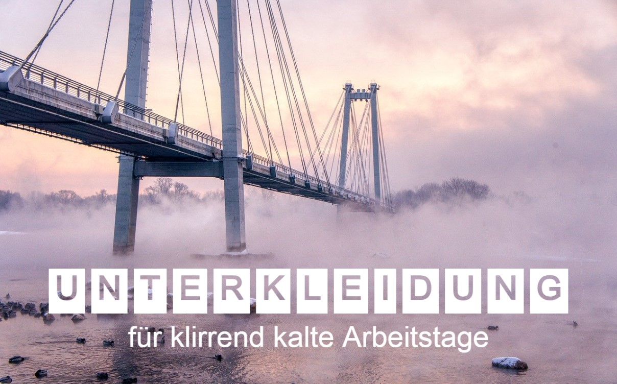 Eine Hängebrücke, die über einen nebligen, zugefrorenen Fluss führt, aufgenommen bei Sonnenaufgang. Der Text "Unterkleidung für klirrend kalte Arbeitstage" ist in großen, weißen Buchstaben über das Bild gelegt. Die Szene vermittelt eine winterliche, frostige Atmosphäre. Ein Link zu unserer Unterkleidung ist hinterlegt.